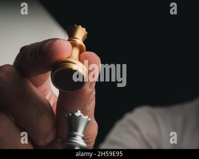 Nahaufnahme des Schachspiels der goldenen Königin in menschlicher Hand mit Kopierraum. Handbewegende Schachfigur der Königin, die bereit ist, die silberne Königin beim Schachspiel anzugreifen Stockfoto