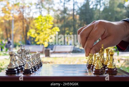 Outdoor-Schachspiel. Schachbrett mit Figuren, Nahaufnahme, Hand macht den ersten Zug. Selektiver Fokus. Stockfoto