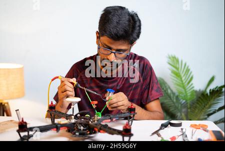 Junger Mann oder Student Drohne durch Löten Drähte zu Hause zu boord - Konzept der Drohne Reparatur und Entwicklung, wissenschaftliche Experimente oder Stockfoto