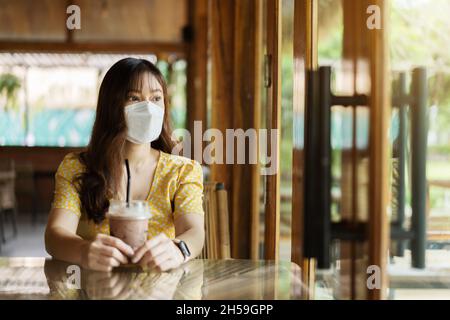 Junge Frau trägt Gesichtsmaske zum Schutz Coronavirus (covid-19) und Trinken Schokoladenmilch im Café Stockfoto
