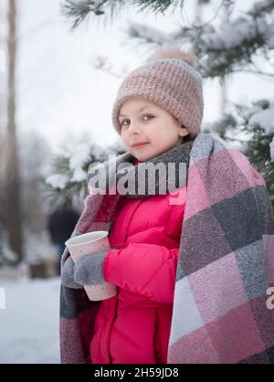 Kleines Mädchen in eine Decke eingewickelt trinken Tee in der Winterwald Stockfoto