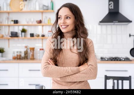 Headshot Porträt einer glücklichen lächelnden Frau, die zur Seite schaut, die in der Küche zu Hause steht Stockfoto