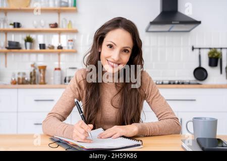 Porträt einer glücklichen, lächelnden kaukasischen Frau, die am Tisch sitzt und die Kamera anschaut Stockfoto