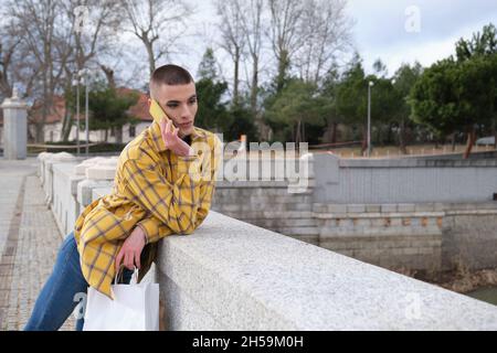 Junger Mann mit Make-up auf dem Smartphone mit Einkaufstaschen sprechen. Stockfoto