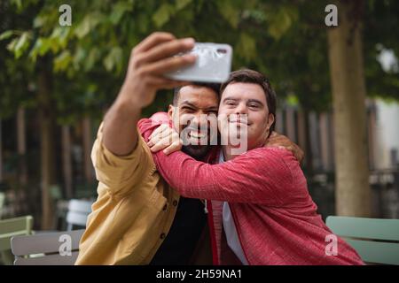 Junger Mann mit Down-Syndrom und sein Mentoring-Freund sitzen und Selfie im Café Stockfoto