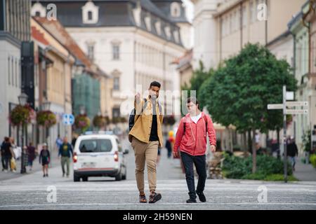 Junger Mann mit Down-Syndrom und sein Mentor-Freund gehen und reden im Freien Stockfoto