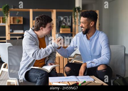 Junger glücklicher Mann mit Down-Syndrom und seinem Mentoring-Freund, der in der Schule Erfolge feiert. Stockfoto