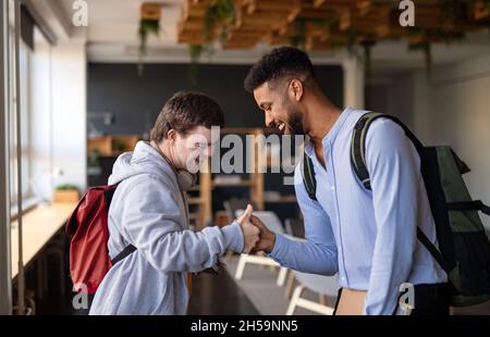 Junger glücklicher Mann mit Down-Syndrom mit seinem Mentoring-Freund, der in der Schule drinnen begrüßt. Stockfoto