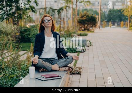 Ruhige Geschäftsfrau, die im Lotos im Freien meditiert, friedliche freiberufliche Mitarbeiterin, die Yoga praktiziert Stockfoto