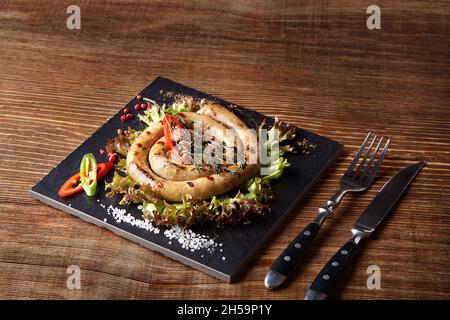 Gebackene hausgemachte Wurst aus nächster Nähe auf einem schwarzen Brett, auf Holzhintergrund. Stockfoto