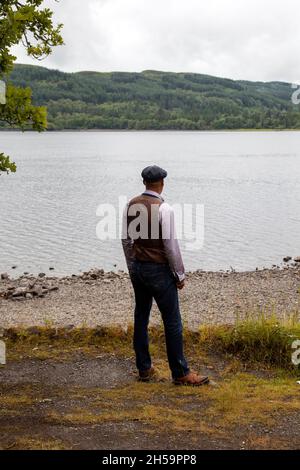 Mann in Weste und Jeans, der am See steht Stockfoto