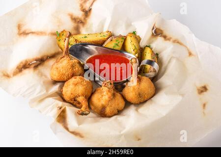 Gebratene Hühnerschenkel paniert und Kartoffel mit Sauce auf einem Blatt Pergament Stockfoto