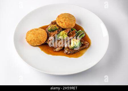Rinderbacken in Sauce mit Brokkoli und grünen Bohnen auf einem weißen Teller. Stockfoto