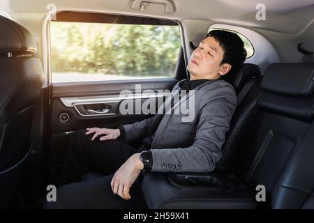 Junger Geschäftsmann schläft, während er auf dem Rücksitz des Autos sitzt Stockfoto