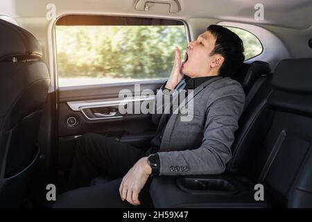 Ein verrummter junger Geschäftsmann, der auf dem Rücksitz des Autos gähnt Stockfoto