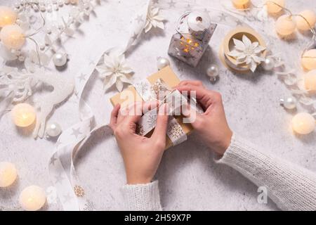 Damenhänden schmücken Weihnachtsgeschenk mit einem weißen Band und Dekor. Vorbereitung auf Weihnachten und Neujahr. Stockfoto