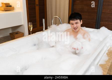 Junger Mann, der Körper wascht und Schaumstoff in der Badewanne spielt Stockfoto