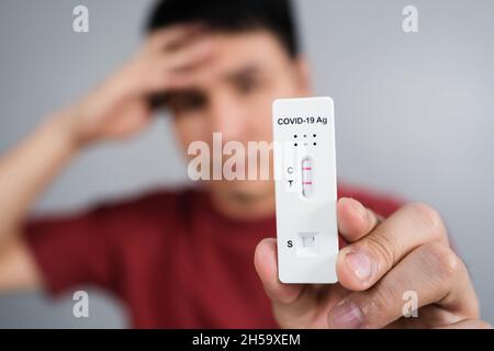Junger gestresster Mann mit positivem Coronavirus(Covid-19)-Testergebnis mit Antigen-Schnelltest-Kit (ATK) Stockfoto