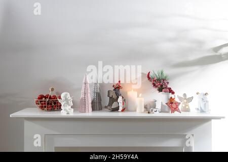 Dekoration des Innenraums der Wohnung zu Weihnachten. Eine Girlande aus geschnitzten Holzfiguren. Kerzen und Keramikfiguren auf einem künstlichen Kamin. Kopie en Stockfoto