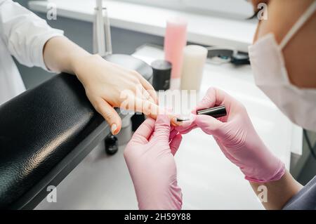 Junge Frau bekommt Maniküre im Schönheitssalon. Manikurist bedeckt die Nägel mit einer transparenten Basis aus Lack. Stockfoto