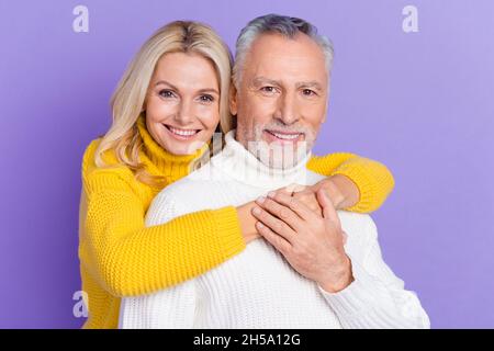 Foto von verträumten charmanten Senior Mann Frau gekleidet Strickmode Pullover umarmt lächelnd isoliert violetten Hintergrund. Stockfoto