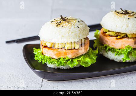 Reisburger mit Lachsschnitzel, Avocado und Sojasauce, grauer Hintergrund. Stockfoto