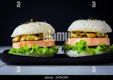 Reisburger mit Lachsschnitzel, Avocado und Sojasauce, schwarzer Hintergrund. Stockfoto