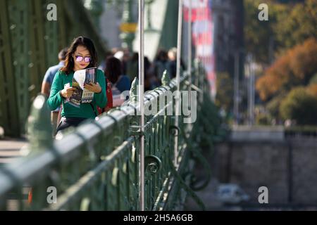 Frau, die die Freiheitsbrücke in Budapest überquert, während sie einen Reiseführer liest Stockfoto