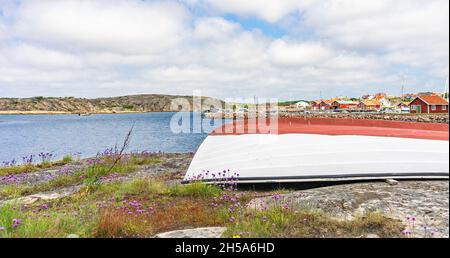 Smögen, Schweden - 9. Juni 2021: Verlassene weiße und rote Boote am Anfang der Insel mit einer Bucht im Hintergrund Stockfoto