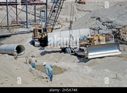 Bauarbeiten am Wellton-Mohawk-Kanal in der Nähe von Yuma, Arizona, USA, in den frühen 1950er Jahren. Hier legen die Arbeiter mit einem Kran die Betonrohre, die das Wasser an einer der Pumpstationen entlang des Kanals heben. Das Wellton-Mohawk Bewässerungs- und Entwässerungsgebiet liegt im Südwesten von Arizona, östlich von Yuma, das zwischen 1949 und 1957 erbaut wurde. Es ermöglicht die Bewässerung im Lower Gila Valley mit Wasser vom Colorado River über den Gila Canal zum Wellton-Mohawk Canal, wo es etwa 160 Meter bis zum Quellwasser gepumpt wird – ein Vintage-Foto aus den 1950er Jahren. Stockfoto