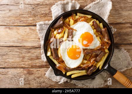 Traditionelle chilenische Chorrillana aus Fries mit Rindfleisch, karamellisierten Zwiebeln und Spiegeleiern in der Pfanne auf dem Tisch. Horizontale Ansicht von oben Stockfoto