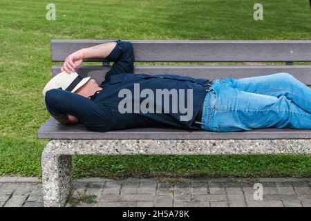 Ein Mann ruht auf einer Bank in einem öffentlichen Stadtpark und bedeckt seinen Kopf mit einem Hut. Das Konzept des Neustarts, der Veränderung oder des Rücksetzens Ihres Lebens und Makins Stockfoto