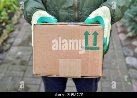 Der Lieferer hält ein Paket mit einem zerbrechlichen Symbol auf einem Karton. Lieferung des Paketkurierdienstes zu Ihnen nach Hause. Zerbrechliche Elemente werden gesendet Stockfoto