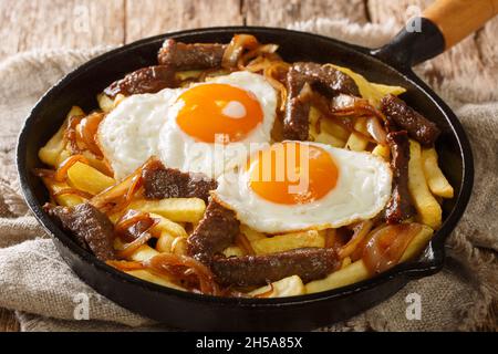 Traditionelle chilenische Chorrillana aus Fries mit Rindfleisch, karamellisierten Zwiebeln und Spiegeleiern in der Pfanne auf dem Tisch. Horizontal Stockfoto