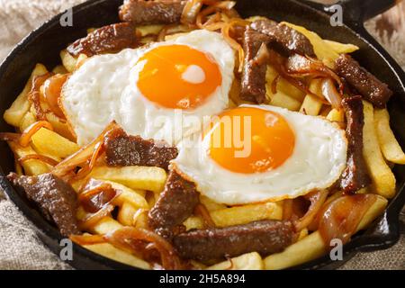 Chorrillana ist ein Gericht, das aus pommes frites mit geschnittenem Fleisch, Spiegeleiern und Zwiebeln in der Pfanne auf dem Tisch besteht. Horizontal Stockfoto