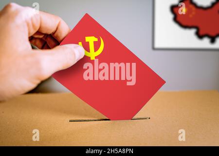 Eine Hand, die eine komunistische Parteiflagge in die Wahlurne legt. Stockfoto