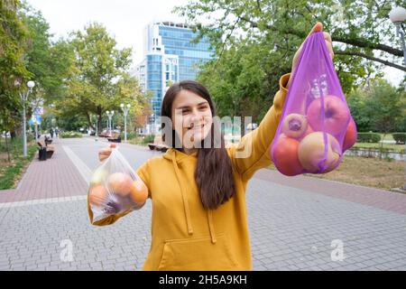 Die Frau hält Gemüse und Obst in einer Plastiktüte und einem Stoffkäufer. Stockfoto