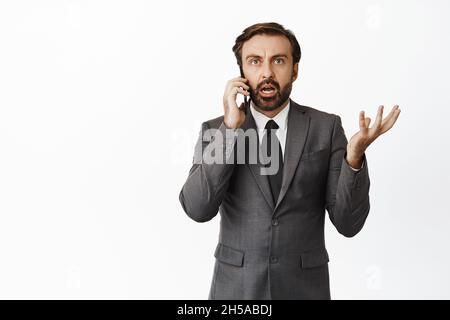Geschäftsmann im Gespräch auf dem Handy mit verwirrten Gesicht, nicht verstehen Anrufer, stand über weißem Hintergrund Stockfoto