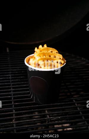 Selektiver Fokus, Pommes frites mit Salz und Gewürzen in einem handgemachten schwarzen imitierten Becher. Low-Key Stockfoto