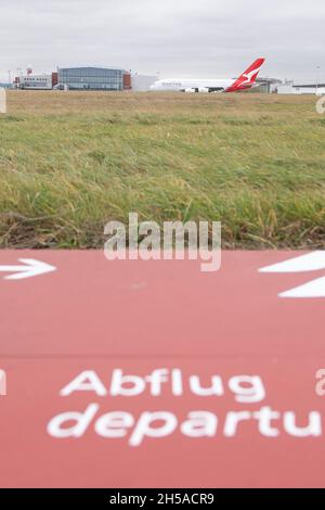 Dresden, Deutschland. November 2021. Ein Qantas Airways Airbus A380 steht vor dem Start am Flughafen Dresden hinter einem Schild mit der Aufschrift „Abflug“. Nach Wartungsarbeiten an den Elbe Flugzeugwerken (EFW) wird das Flugzeug den Langstreckenflug nach Sydney antreten. Quelle: Sebastian Kahnert/dpa-Zentralbild/dpa/Alamy Live News Stockfoto