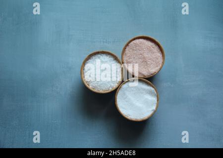 Himalayasalz, feines Salz und grobes Salz in Kristallsteinen in Holzschüsseln auf hellblauem Hintergrund, Draufsicht. Stockfoto