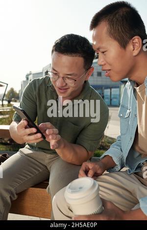 Kleine Gruppe von chinesischen Geschäftsleuten diskutieren Foto oder Video auf dem Smartphone, während sie sich in der städtischen Umgebung ausruhen Stockfoto