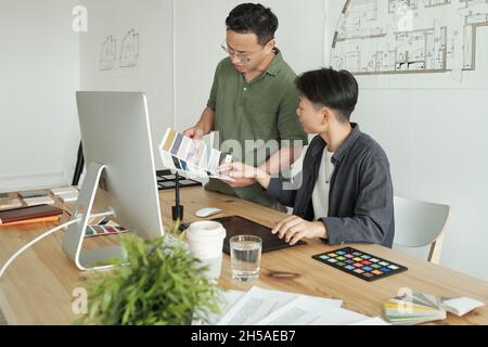 Zwei junge, zeitgenössische Architekten, die sich für die Innenausstattung entscheiden, treffen sich am Arbeitsplatz vor dem Computermonitor Stockfoto