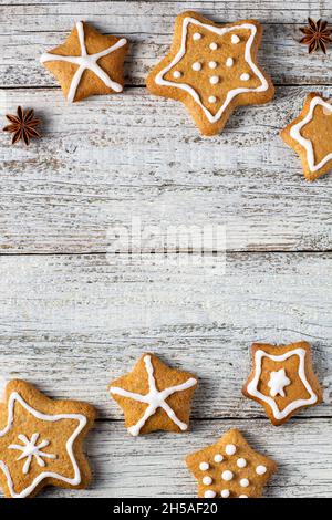 Rand von weihnachtlichen Lebkuchen in Sternform mit Glasur- und Gewürzmustern auf weißem Holzhintergrund. Draufsicht mit Kopierbereich Stockfoto