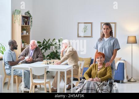 Porträt einer jungen Krankenschwester mit einer älteren Frau, die lächelt vor der Kamera während ihrer Arbeit im Pflegeheim kümmert sie sich um ältere Menschen Stockfoto