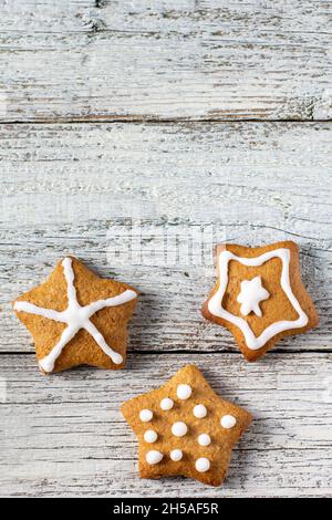 Rand von weihnachtlichen Lebkuchen in Sternform mit Glasur- und Gewürzmustern auf weißem Holzhintergrund. Draufsicht mit Kopierbereich Stockfoto