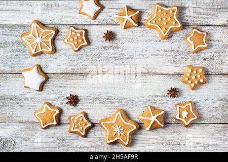 Rahmen aus weihnachtlichen Lebkuchen in Sternform mit Glasur- und Gewürzmustern auf weißem Holzhintergrund. Draufsicht mit Kopierbereich Stockfoto