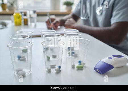 Nahaufnahme einer Brille mit Pillen im Inneren, die im Krankenhaus auf dem Tisch steht und einen Arzt im Hintergrund hat Stockfoto