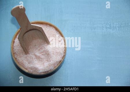 Himalaya-Salz, rosa, in einer Holzschale, mit einem hölzernen Messlöffel auf einem antiken Holztisch. Blick von oben. Stockfoto