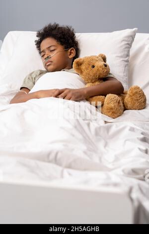 Krankes Kind, das während seiner Behandlung im Krankenhaus mit einem Teddybär auf dem Bett schlief Stockfoto